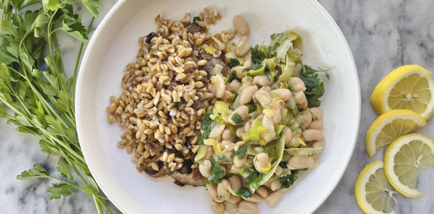 cooked barley grains and cooked white beans garnished with green herbs atop a white dish