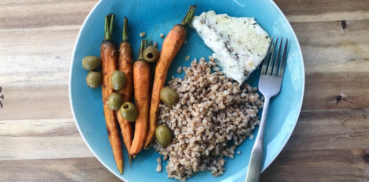 Whole roasted carrots topped with olives, next to a serving of farro grains and a fillet of fish