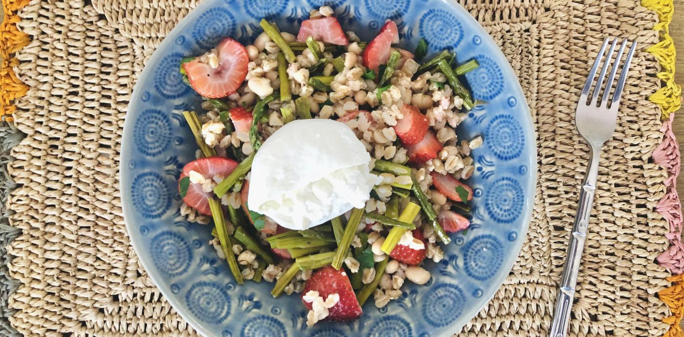 a salad with grains and burrata cheese in a blue bowl on a woven placemat