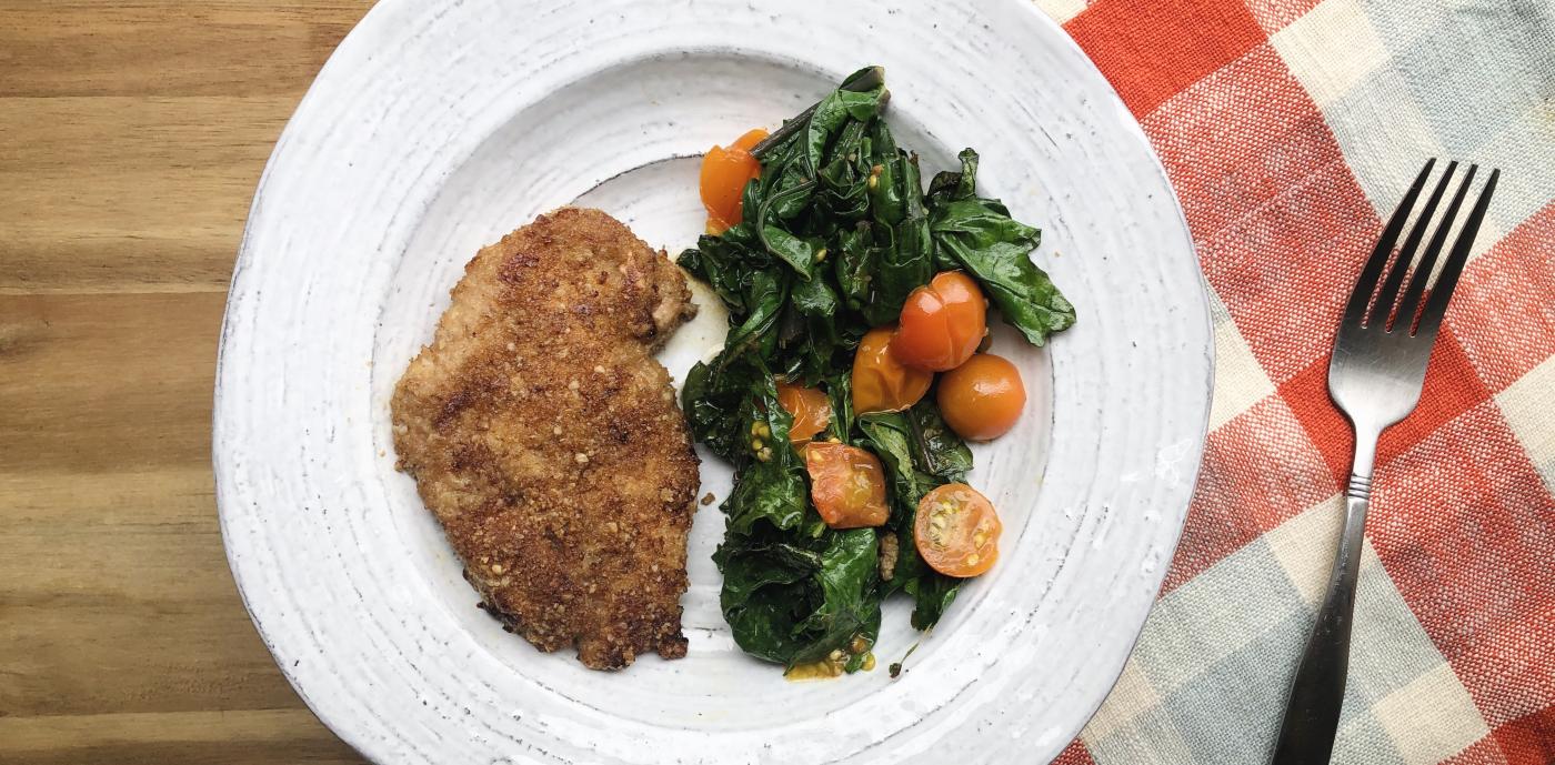 breaded chicken next to cooked greens and tomatoes on a white plate