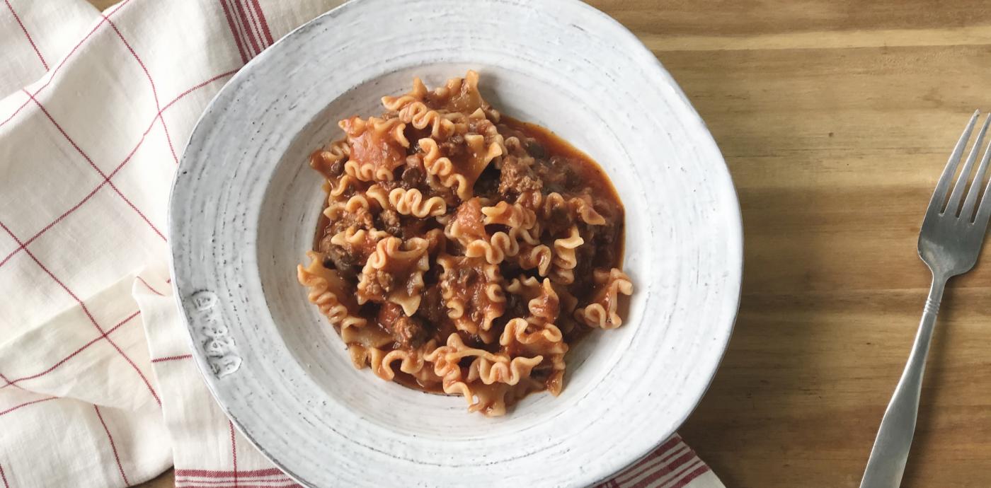 bowl of pasta with tomato meat sauce on a wooden table
