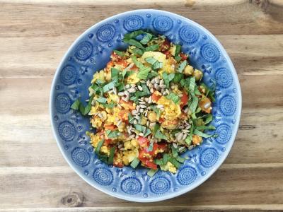 Vibrant yellow couscous salad with red peppers in green basil in blue pottery on a wooden surface