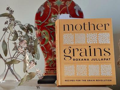 Cover of the cookbook Mother Grains, leaning on red vase with dried flowers