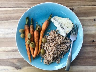 Whole roasted carrots topped with olives, next to a serving of farro grains and a fillet of fish
