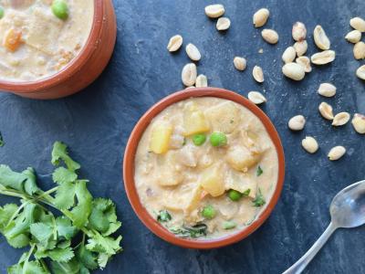 a bowl of creamy soup on a dark backdrop with cilantro and peanuts scattered around