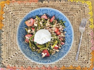 a salad with grains and burrata cheese in a blue bowl on a woven placemat