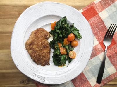 breaded chicken next to cooked greens and tomatoes on a white plate