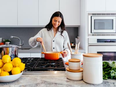 Woman in kitchen stirring a orange pot with wooden spoon 