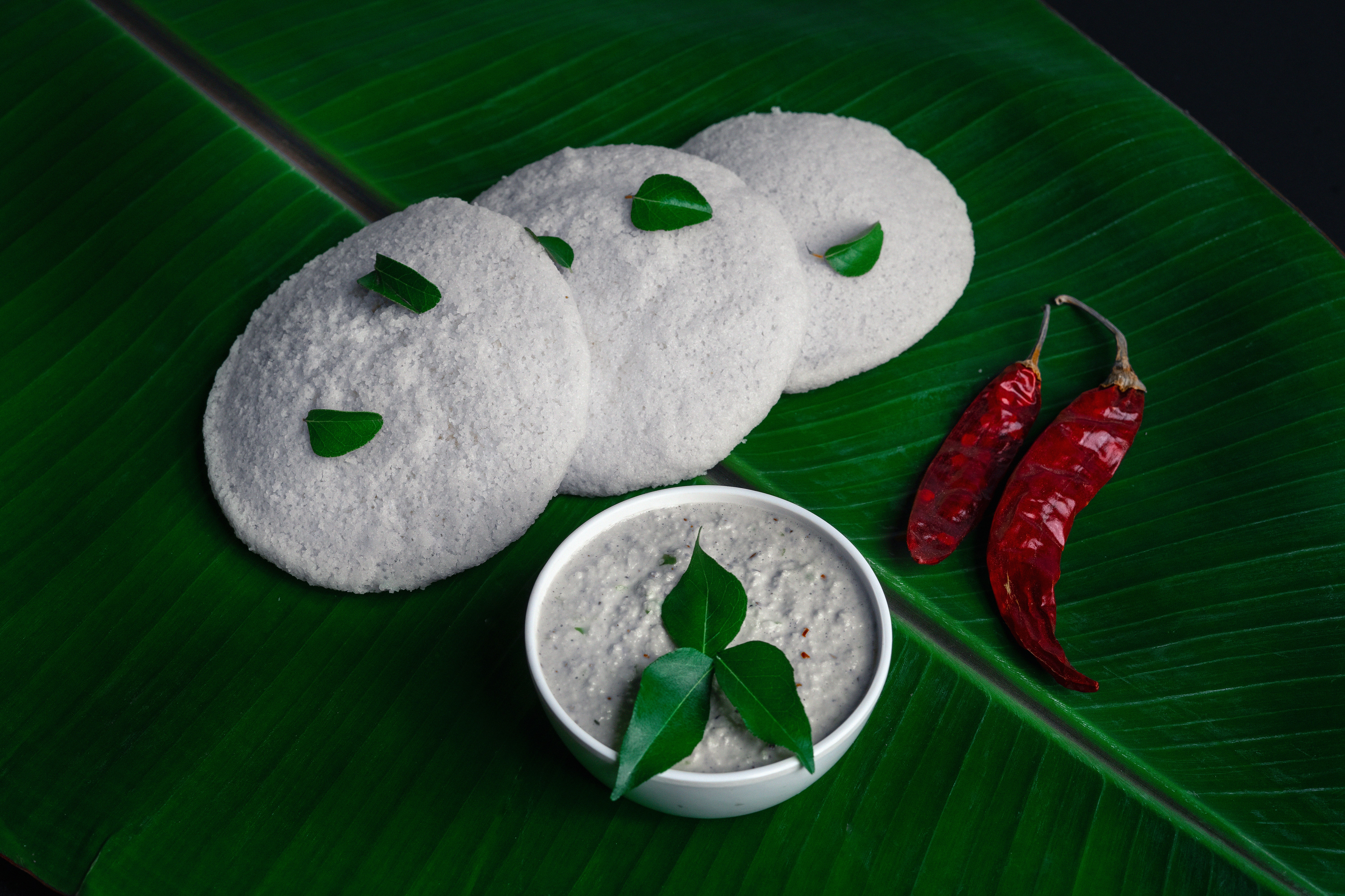 Three idlis on a banana leaf with peppers