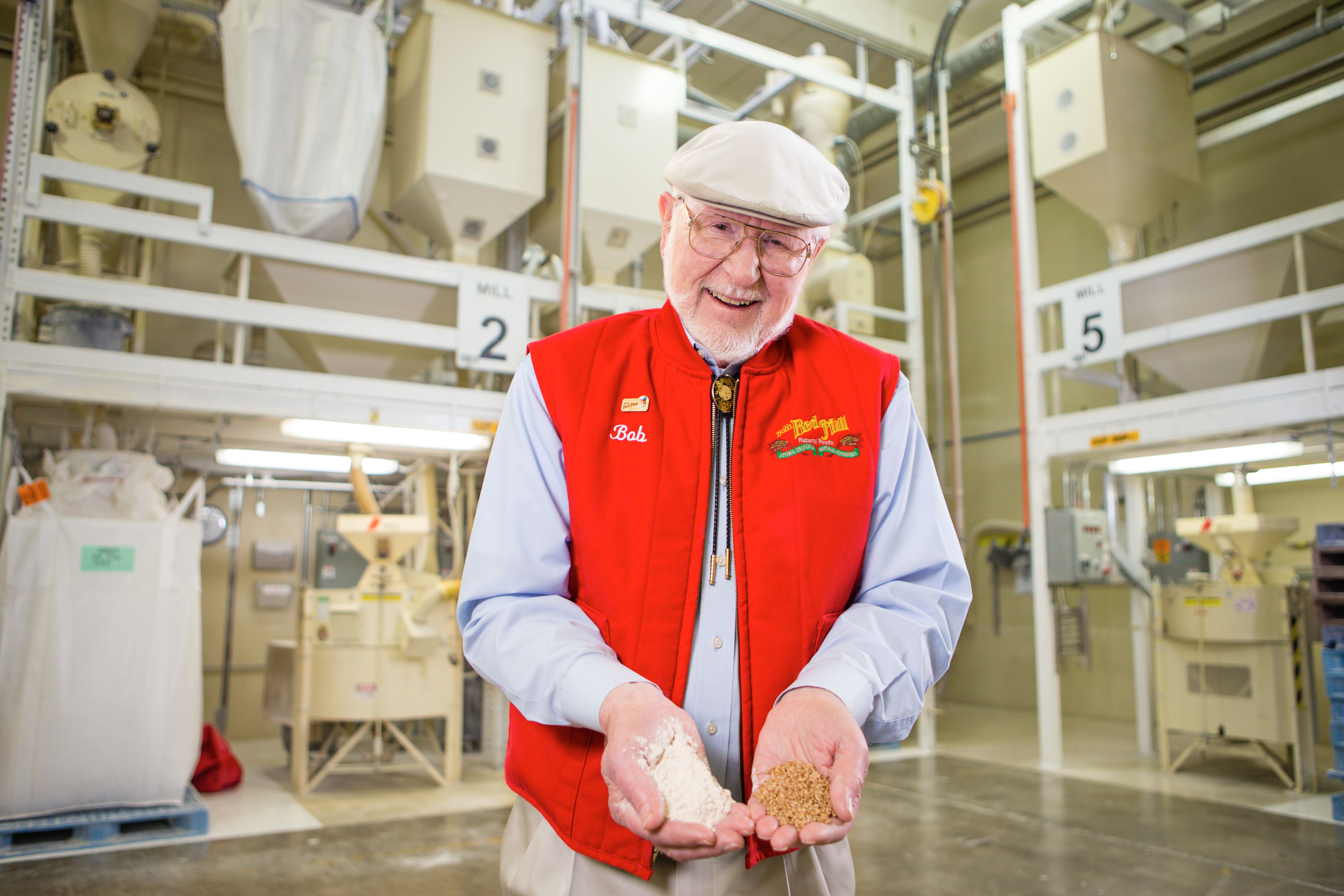 Bob Moore standing in front of milling machinery, holding handfuls of grain