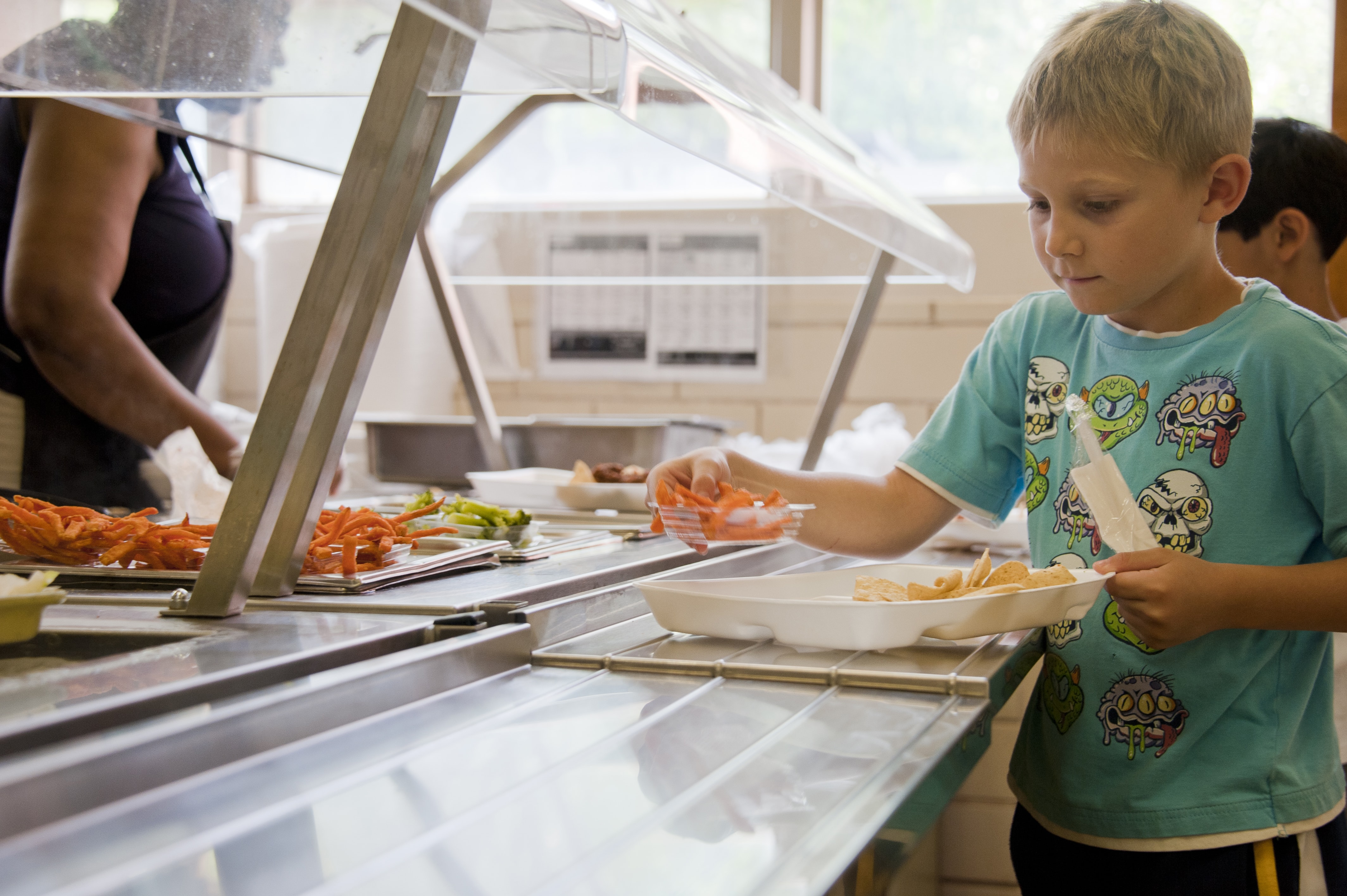 A blond elementary student selecting food in a lunch line