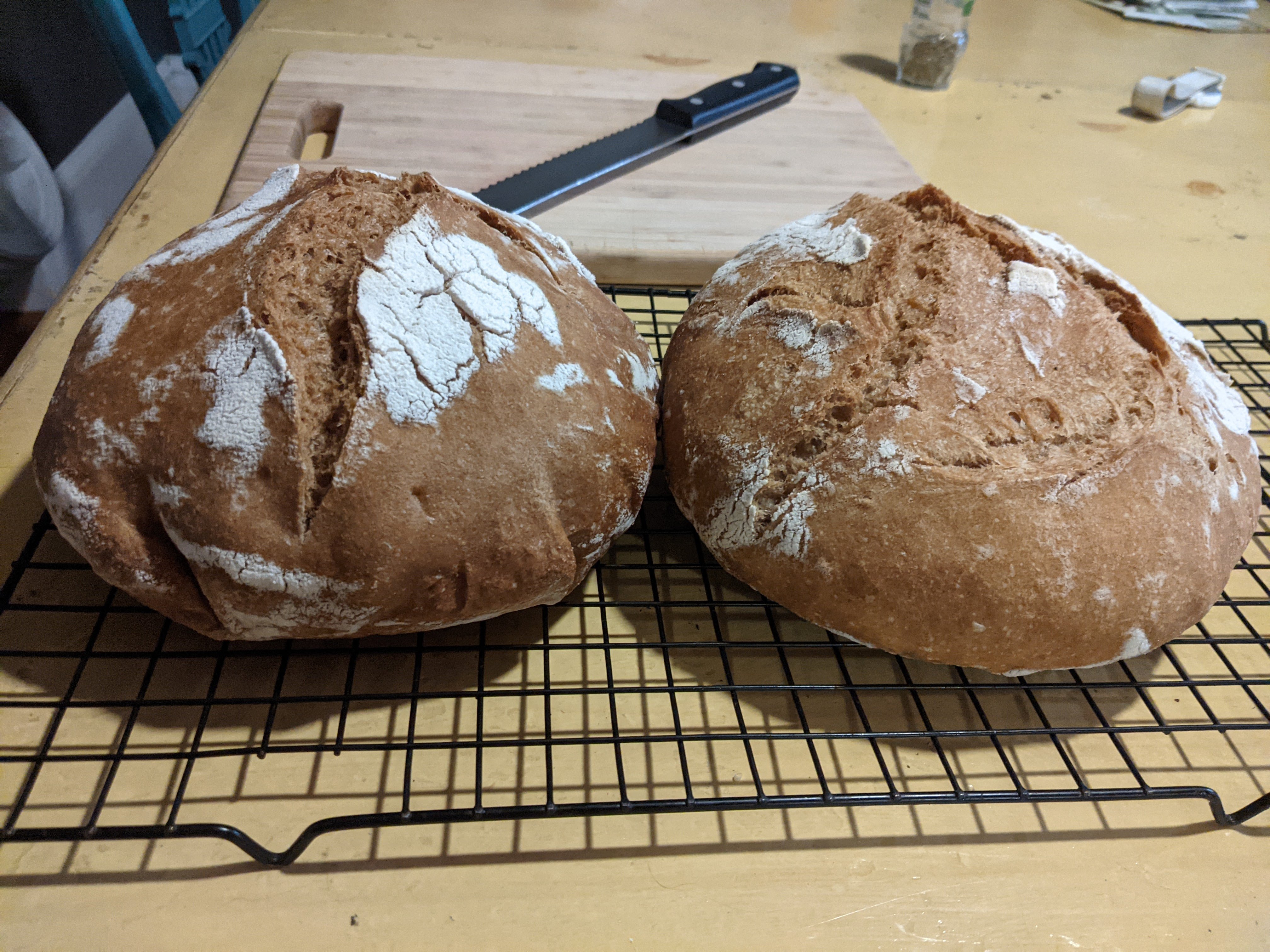 two loaves of bread side by side with cutting board and bread knife in background