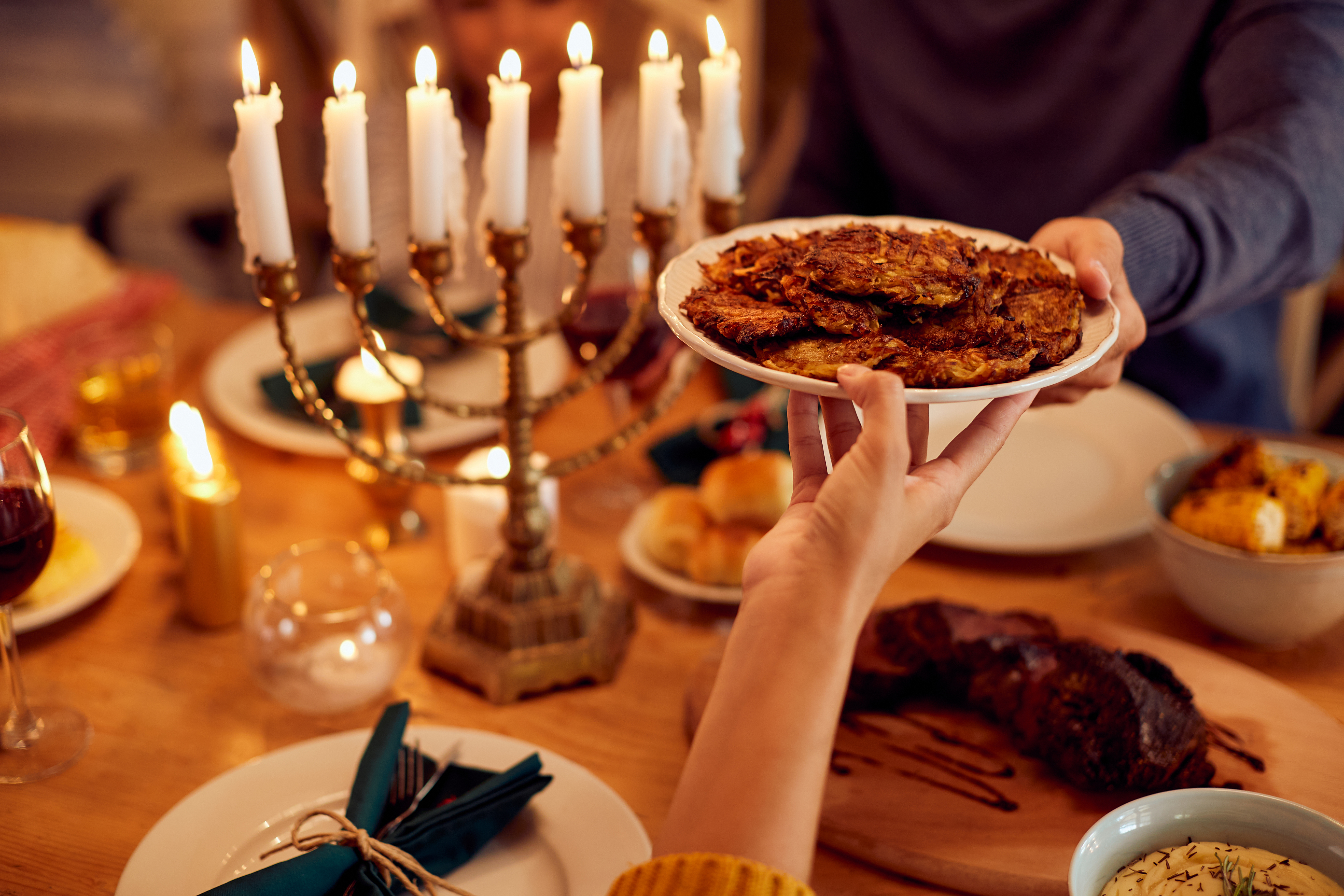 Family passing latkes with a fully lit menorah in the background