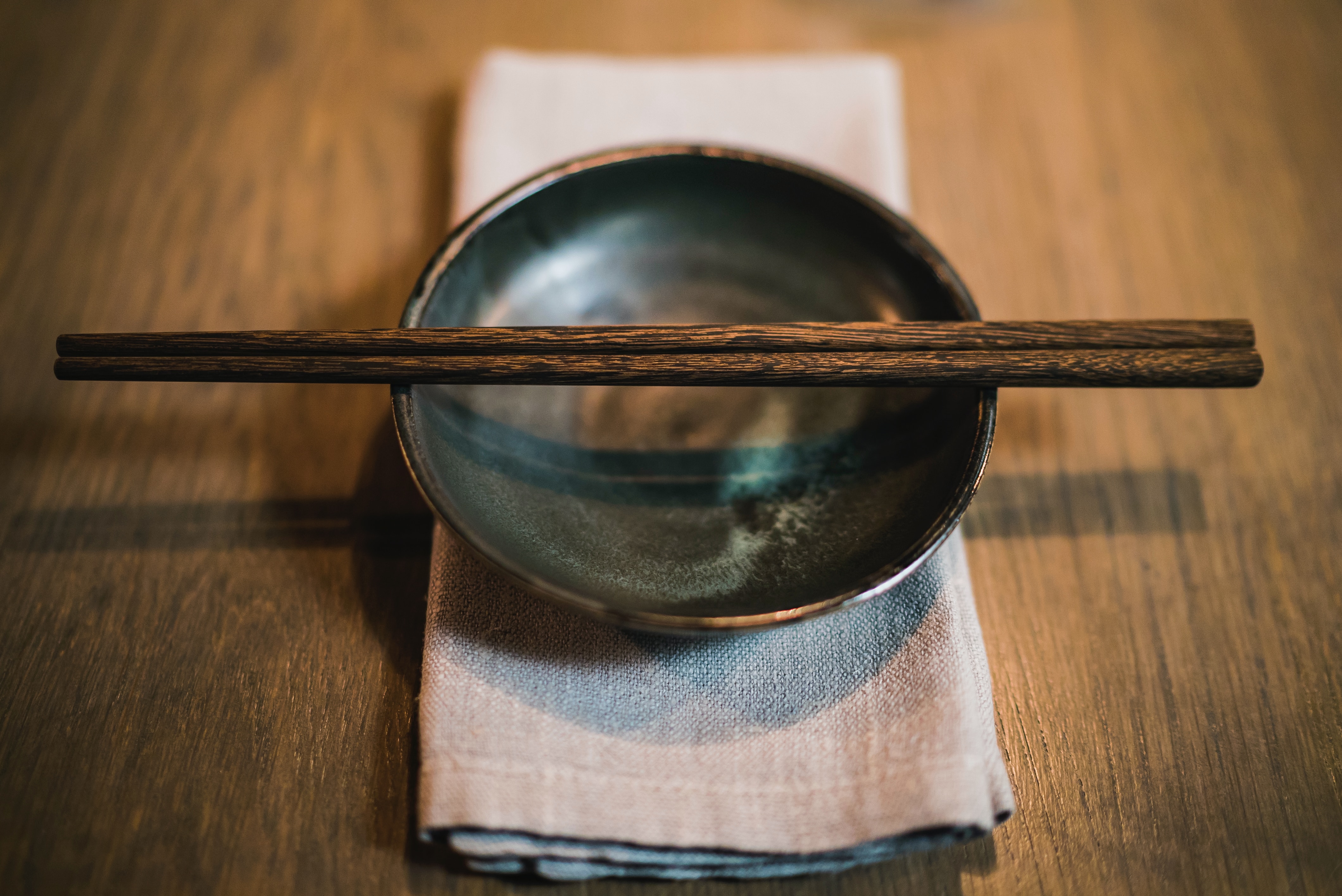 A pair of wooden chopsticks lain across a dark plate, ready to be used